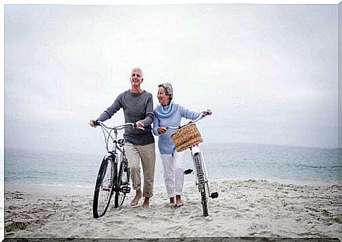 Elderly couple riding a bicycle on the beach fighting loneliness.